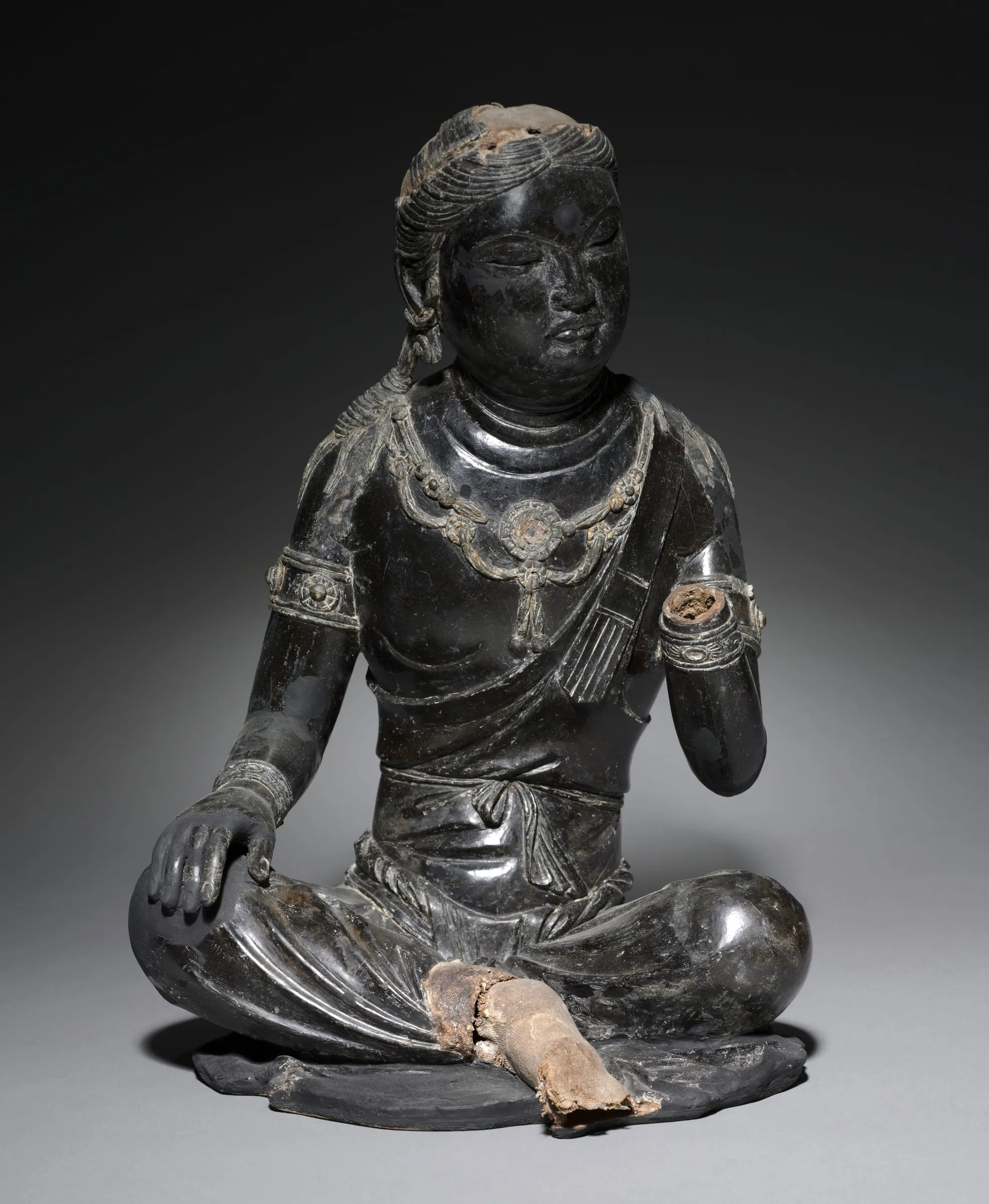 A seated bodhisattva in dark lacquer, wearing jewelled ornaments.