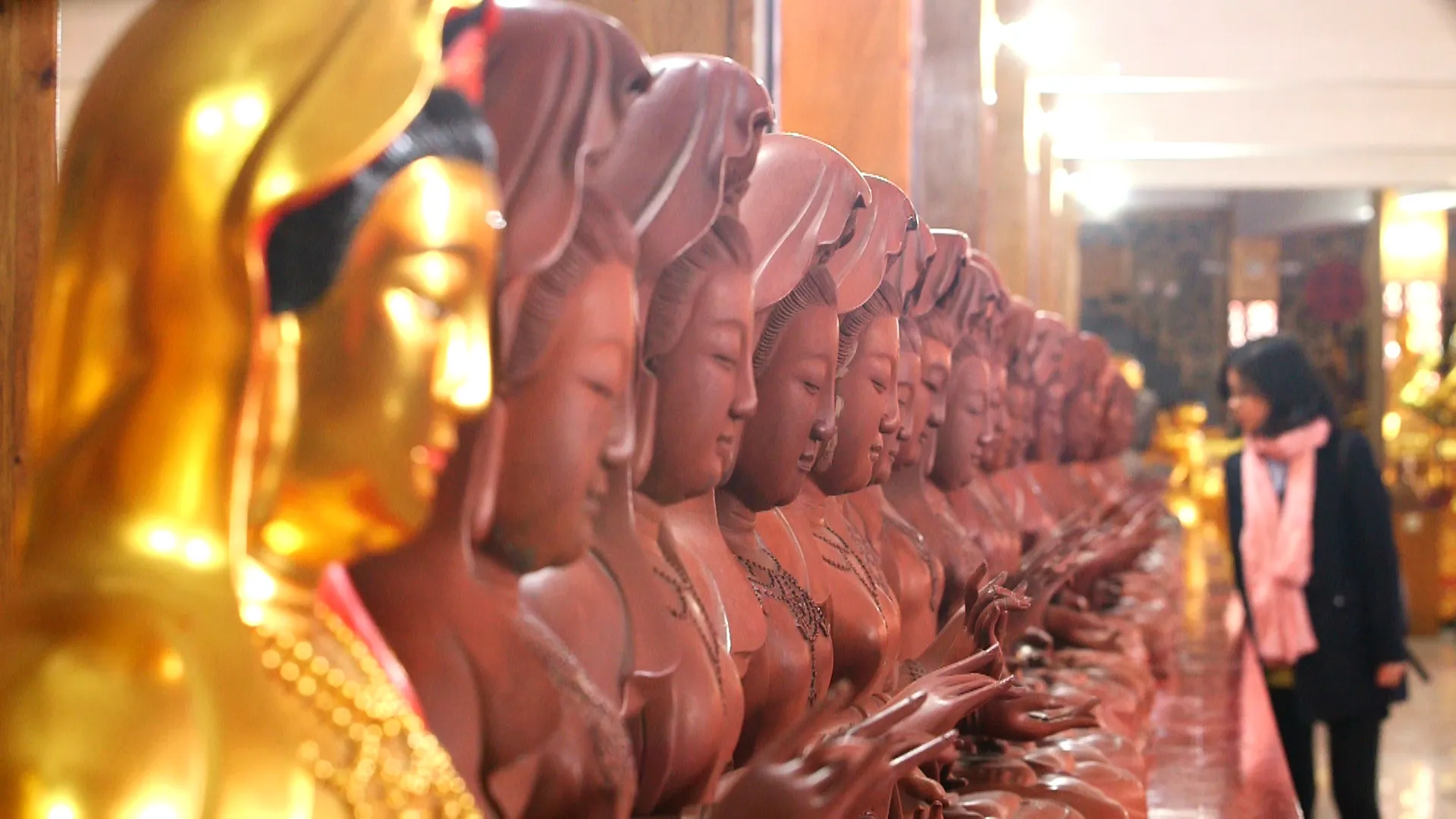 A row of Buddhist sculptures in a workshop, showing reddish-brown surfaces and a gilded figure in the foreground.