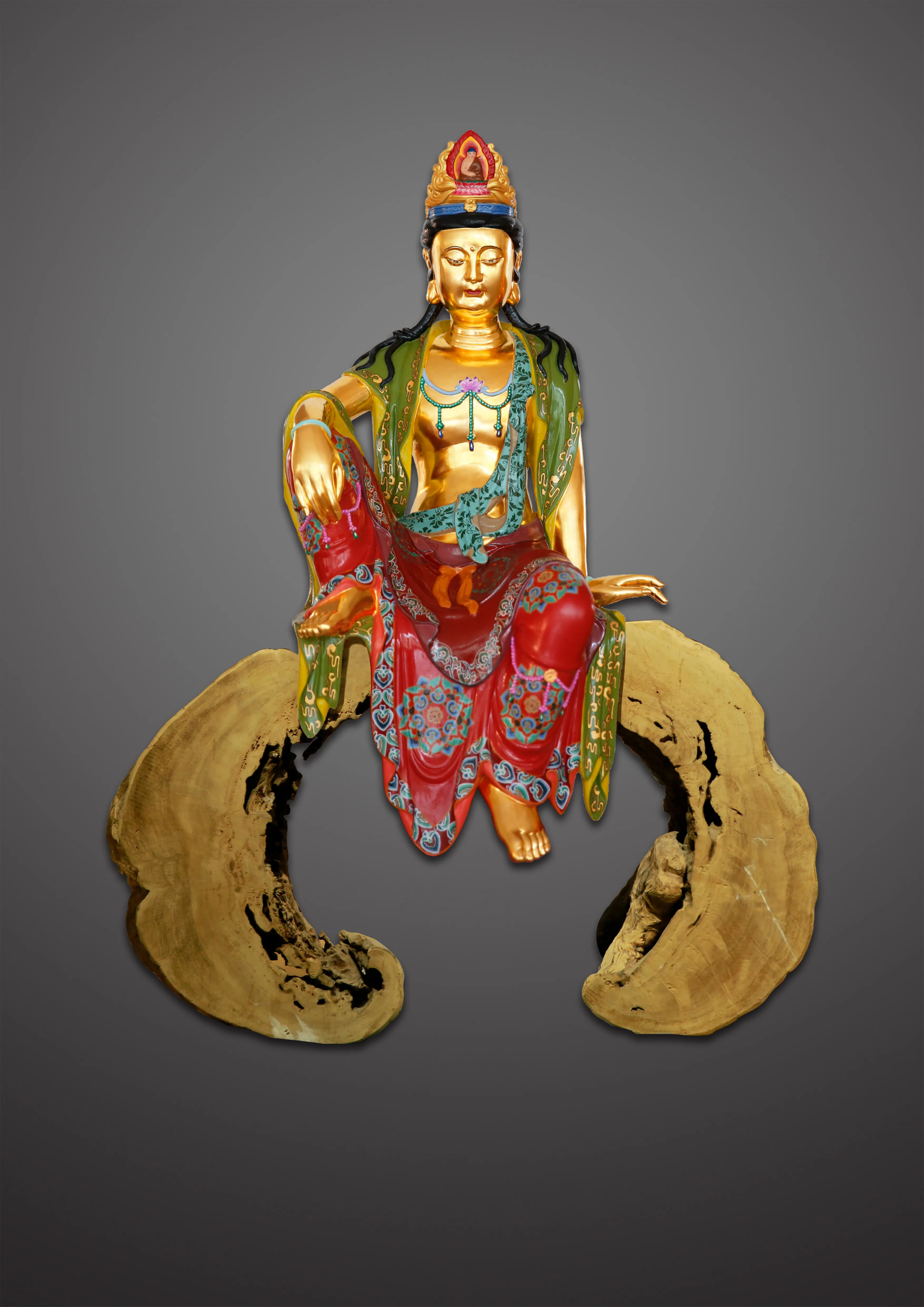 A gilded Guanyin in a green mantle and red robe, seated at ease on a curving wooden base.
