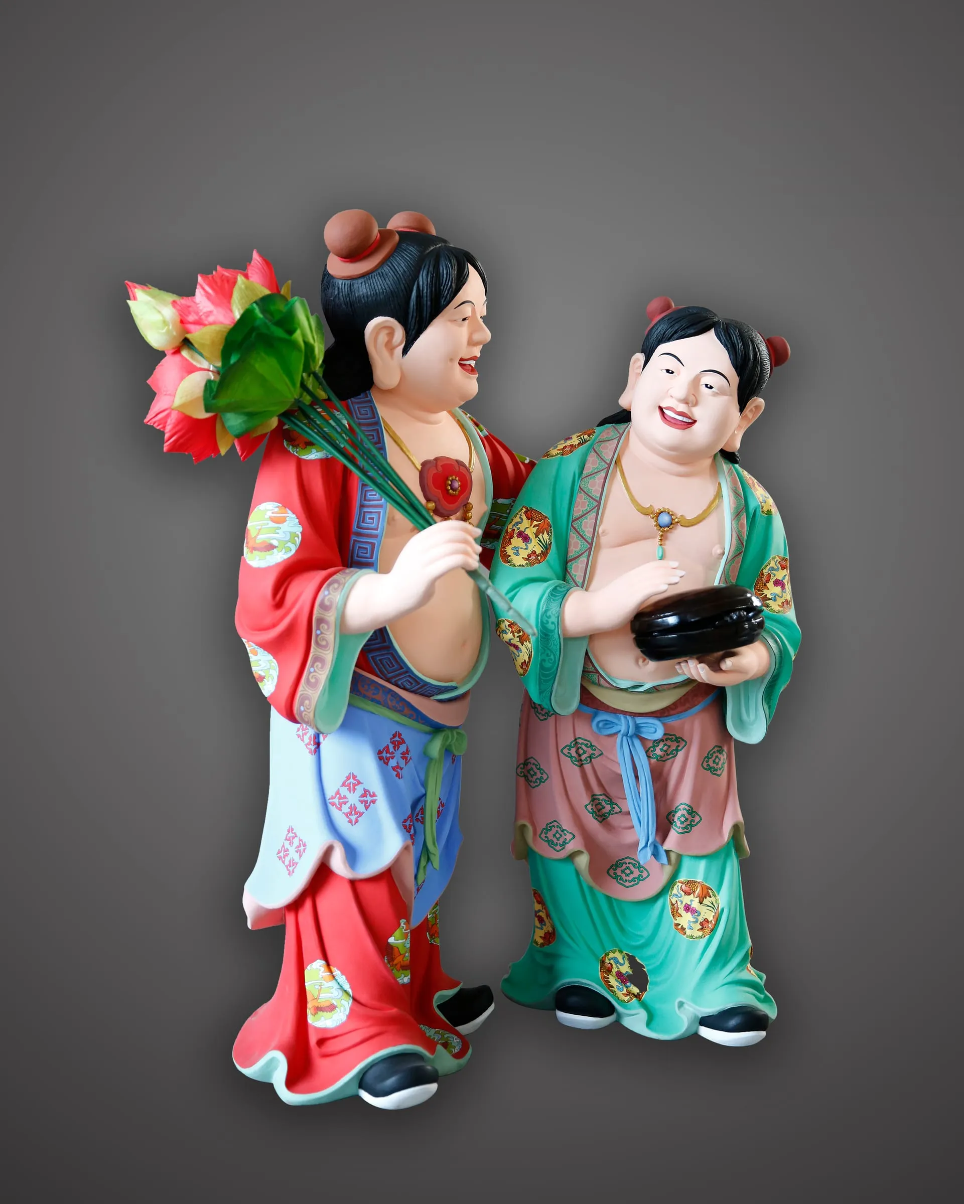 Two smiling boys in painted robes, one holding lotus flowers, the other a box.
