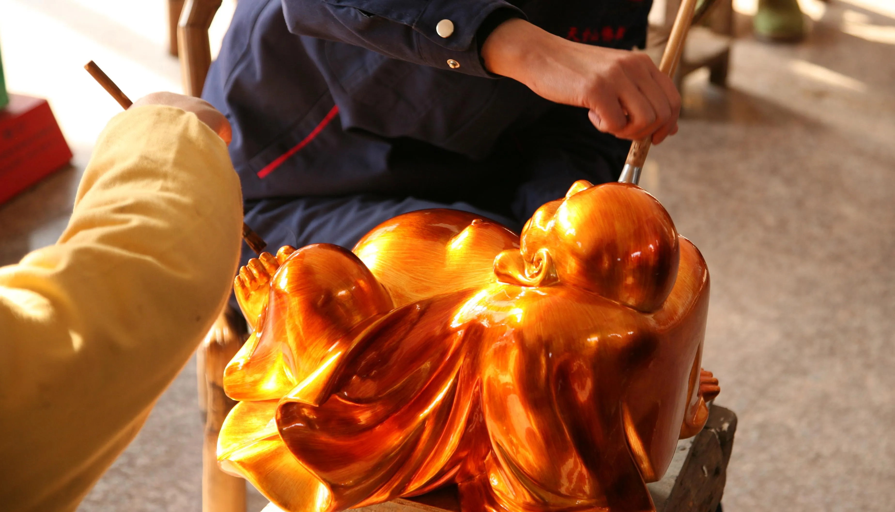 Artisans applying a finish to a Buddhist sculpture.