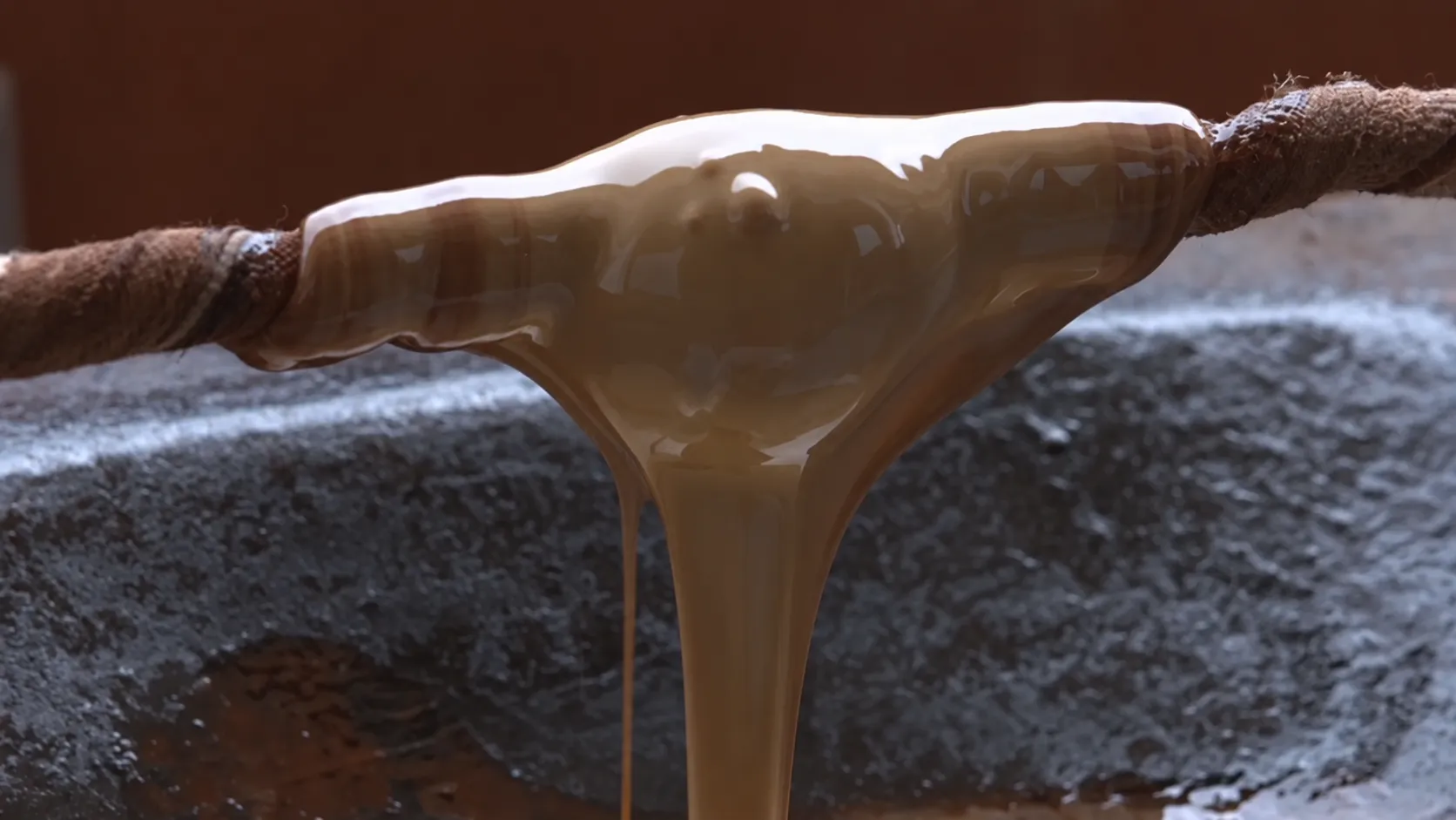 Natural lacquer flowing from a cloth-wrapped stick above a vessel.