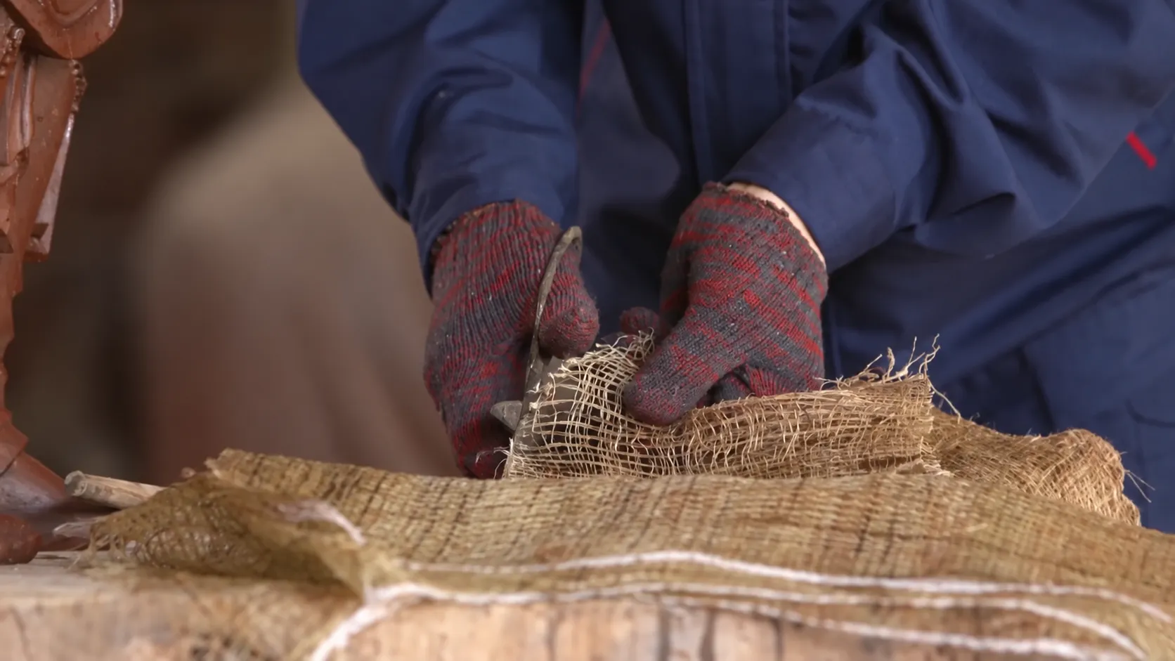 Gloved hands cutting coarse woven textile in a sculpture workshop.