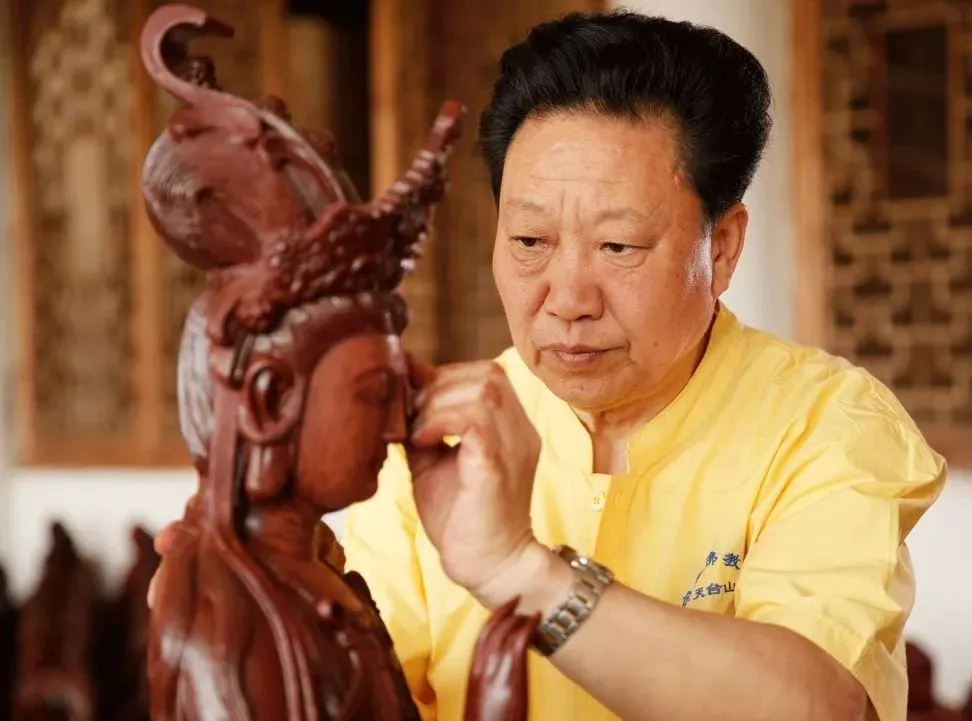 Tang Chunfu, in a yellow work shirt, refining the face of a crowned figure.