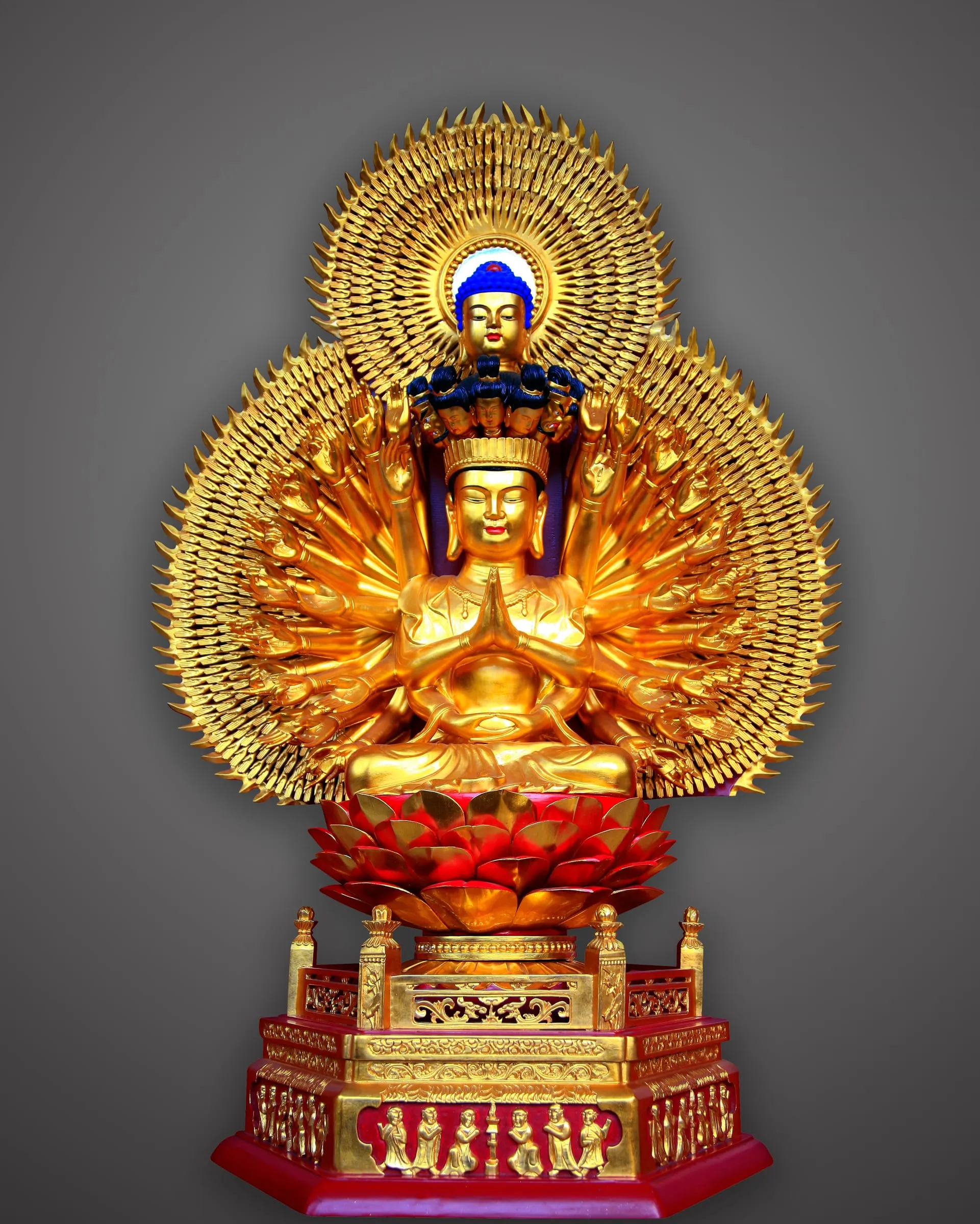 Gilded seated Guanyin ringed by a disc of many arms, on a red and gold base.