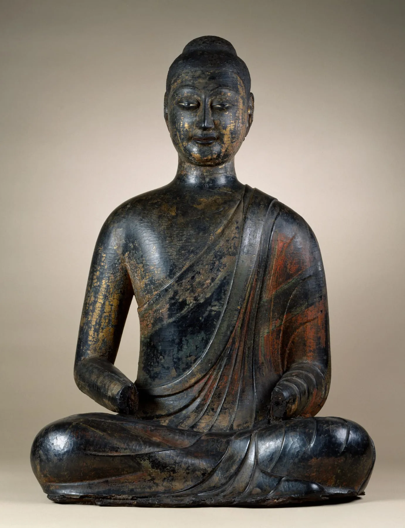 A seated Buddha with a dark, worn lacquer surface; both hands are missing.