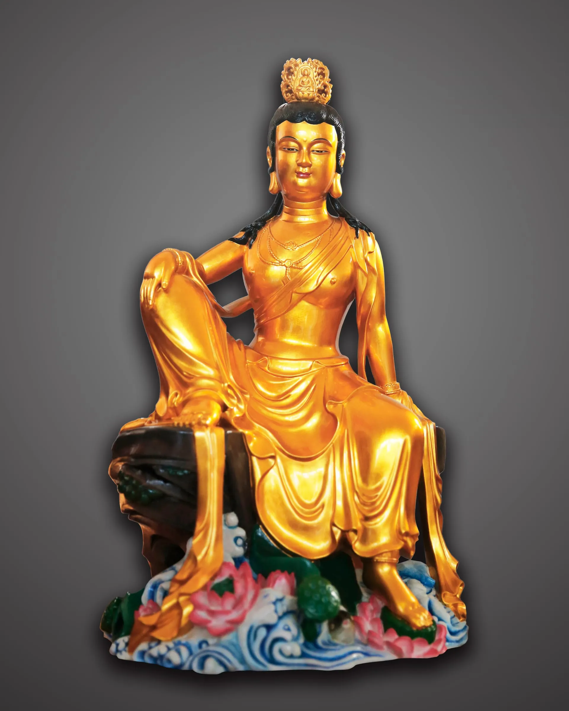Gilded Guanyin seated at ease on rocks above painted waves.